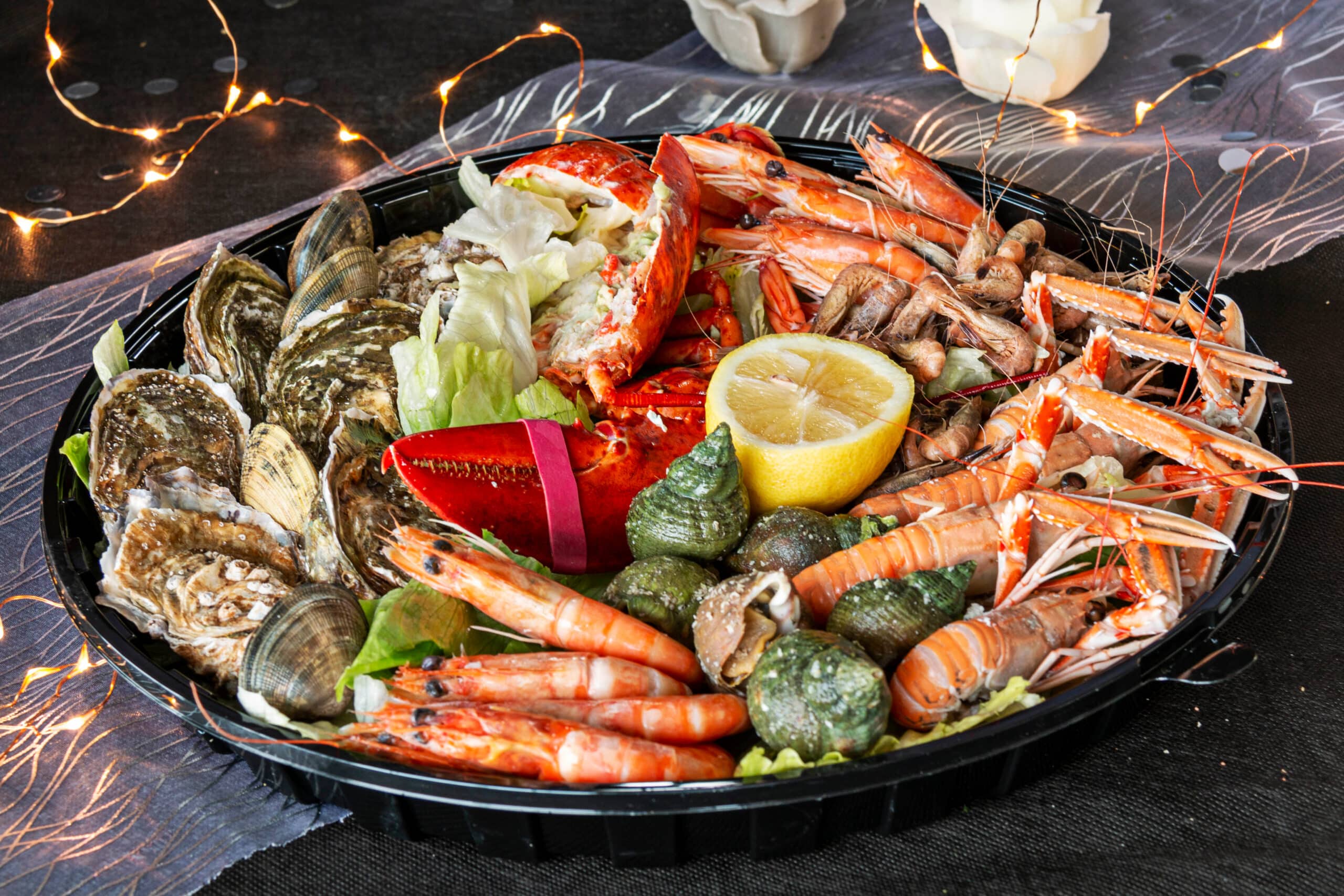 Plateau de fruits de mer festif avec huîtres, homard, langoustines, crevettes, et bigorneaux, décoré de citron et de lumières scintillantes.